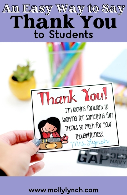 A hand holds a thank you card for students with colorful text, a cartoon teacher, and classroom supplies blurred in the background—perfect for Teacher Thank You Notes.