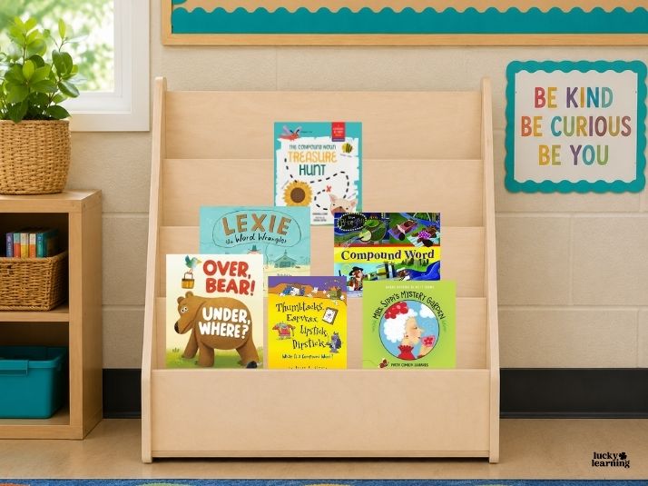 A wooden bookshelf displays six children's books in a classroom. The colorful covers feature fun compound words. A sign on the wall reads, "Be Kind Be Curious Be You.