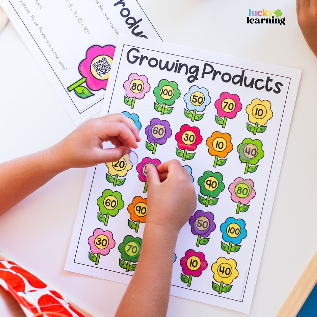 A child places counters on a worksheet titled "Growing Products," featuring colorful flowers, each labeled with a different two-digit number—a playful approach to math fact fluency games.