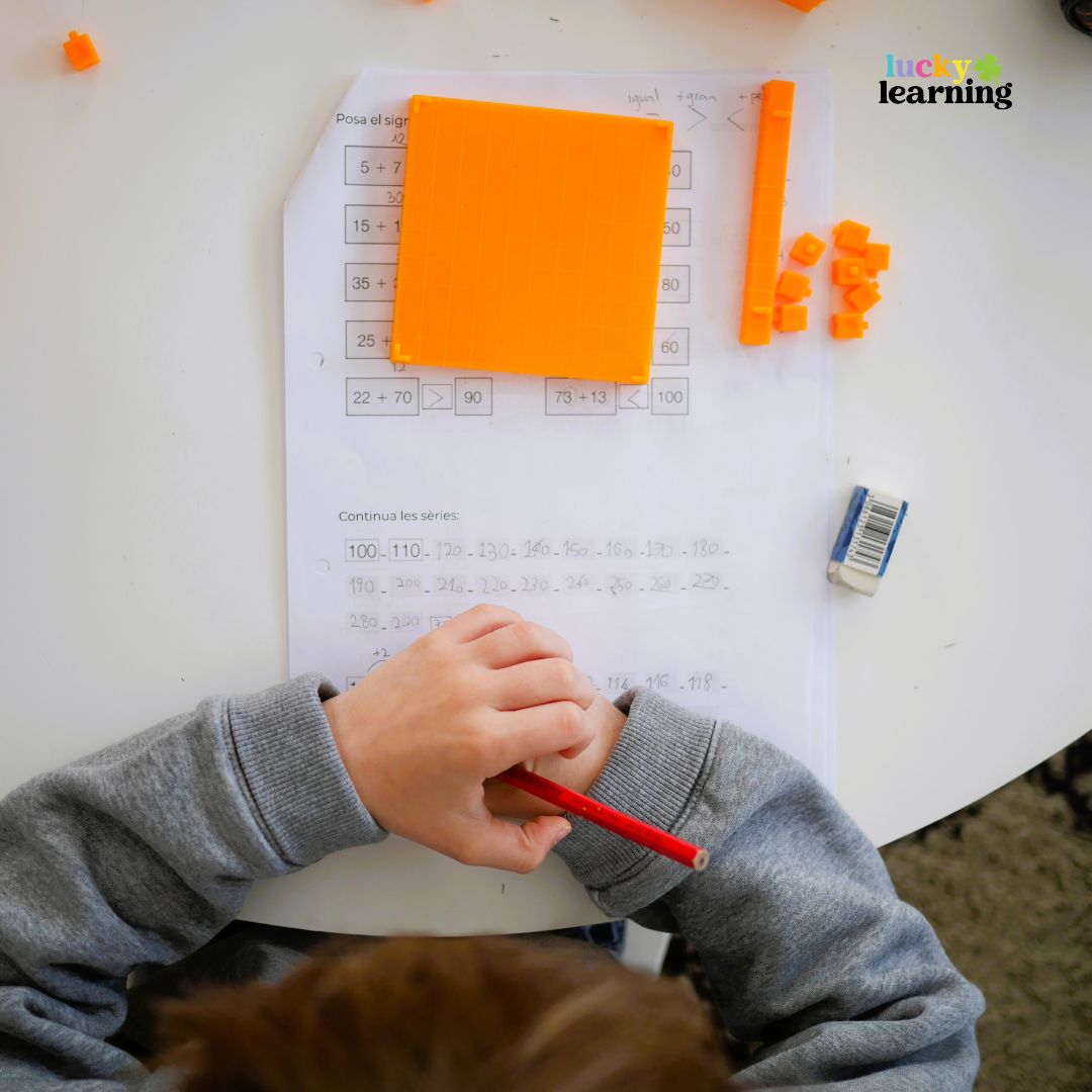 Child working on a math worksheet with orange counting blocks, pencil, and eraser on a white table. "lucky learning" logo in the top right corner highlights fun math fact fluency games for kids.