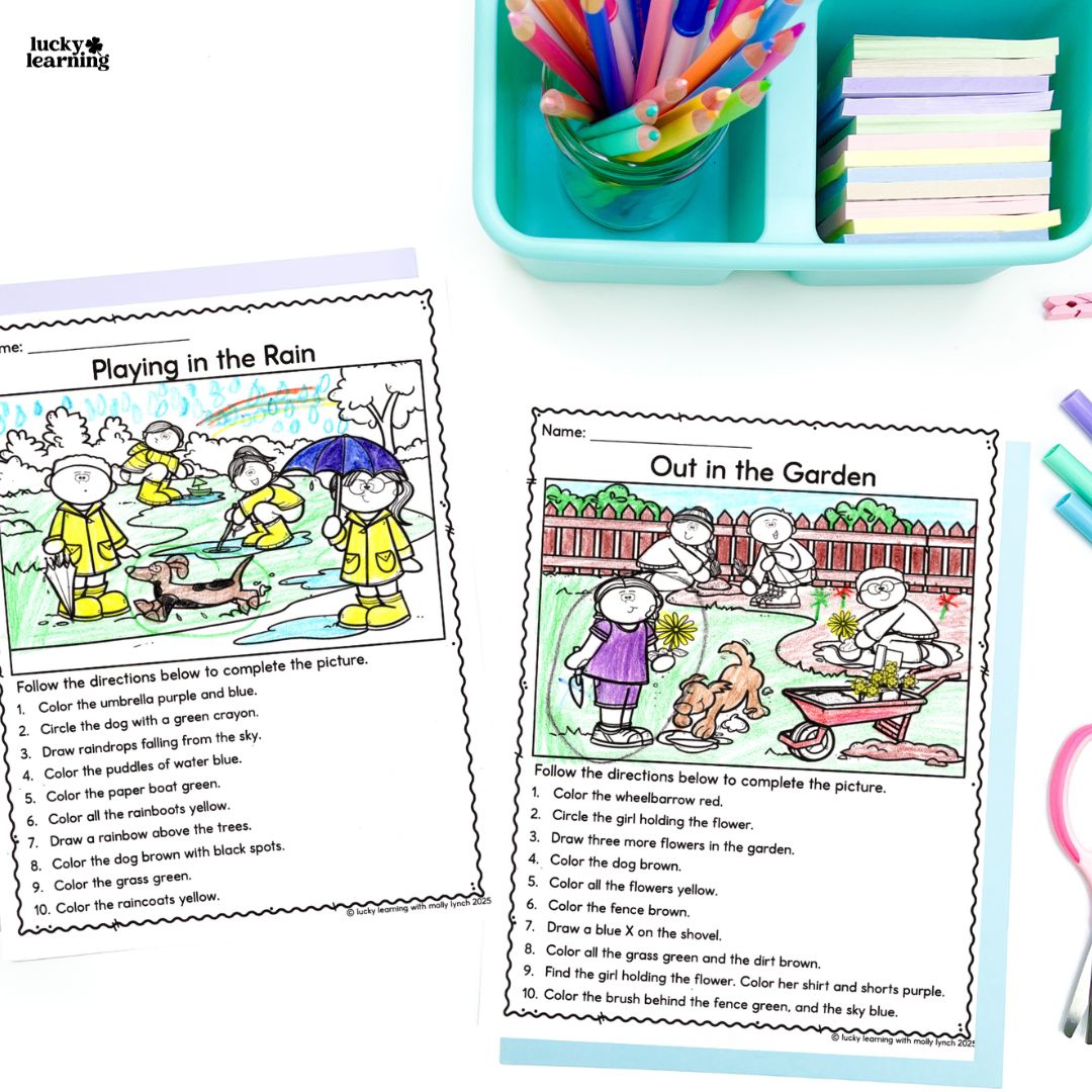 Two colored worksheets titled "Playing in the Rain" and "Out in the Garden" sit on a white table, surrounded by colored pencils, crayons, and a blue supply tray—perfect for practicing following directions.