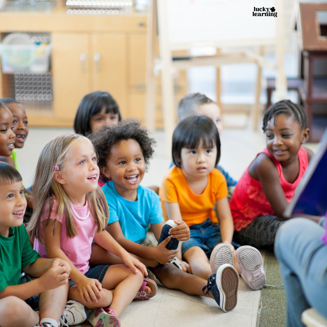 A group of young children sit on the floor in a classroom, attentively listening to an adult reading a book and following directions.
