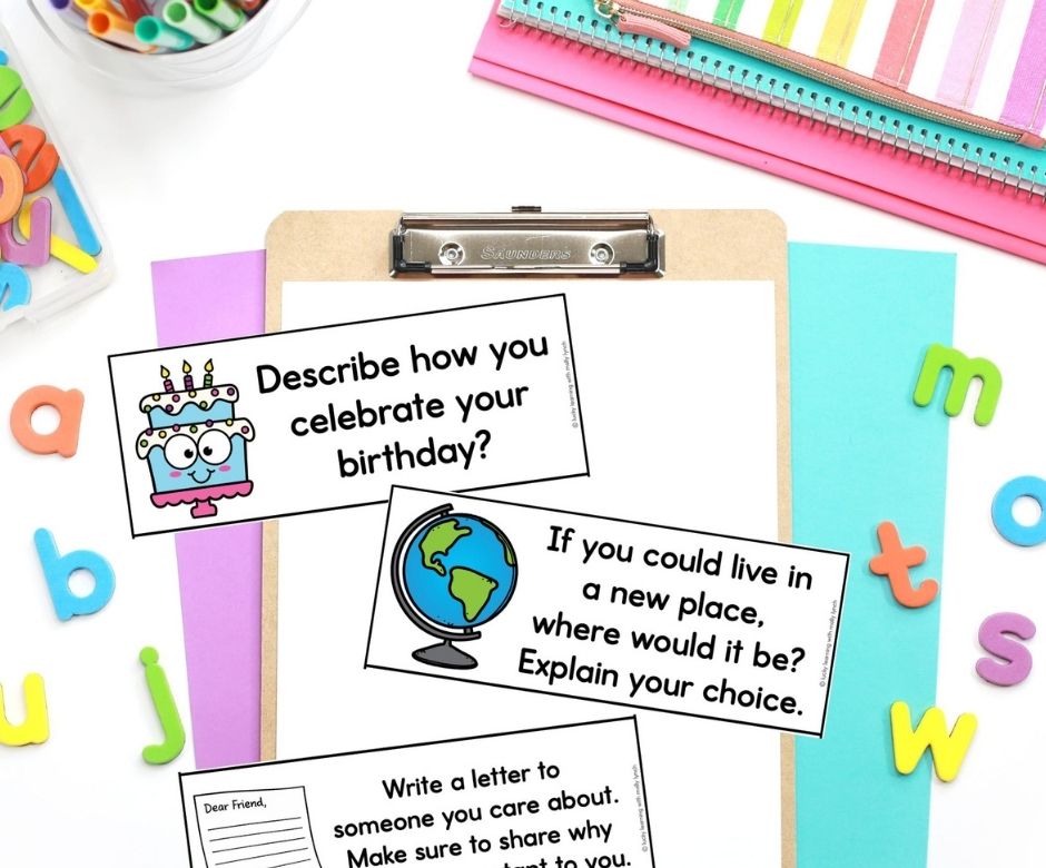 A clipboard with colorful paper and three engaging journal writing prompts for first grade, surrounded by letters, a pencil holder, and a striped pencil case.