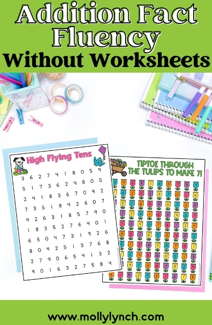 Two colorful fact fluency activity sheets are on a white surface, surrounded by stationery like pens, scissors, tape, and notebooks. Text above reads “Addition Fact Fluency Without Worksheets.”.