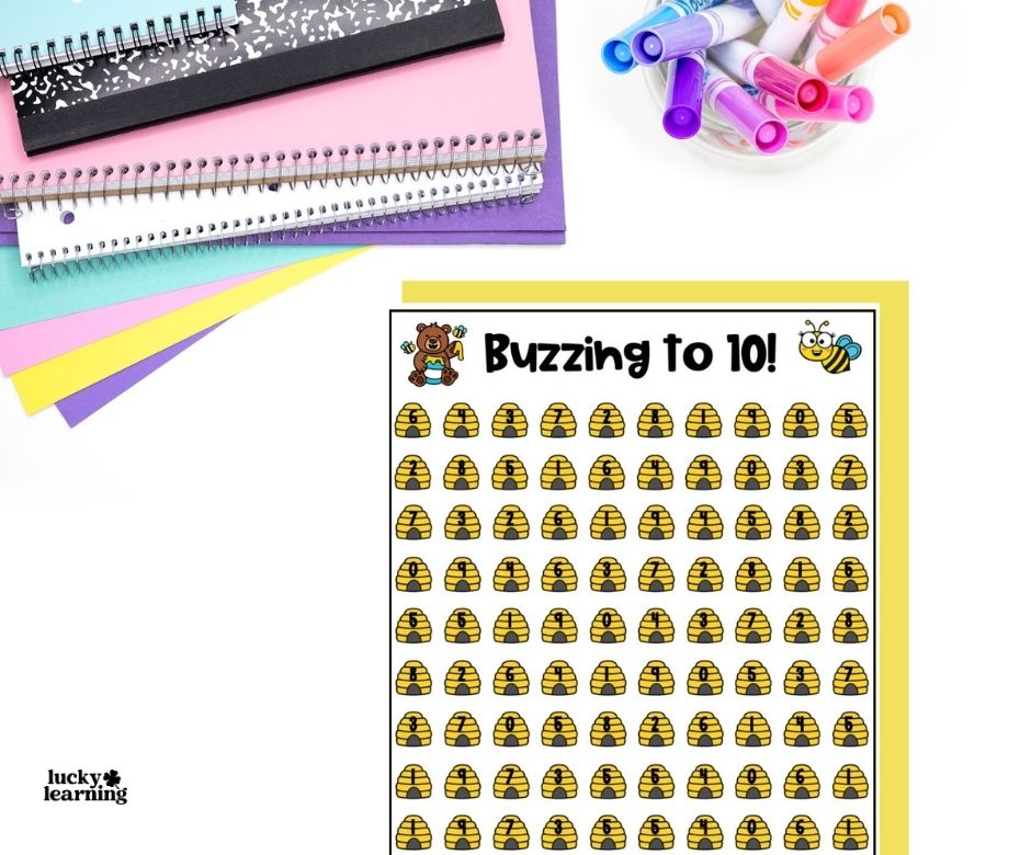 A worksheet titled “Buzzing to 10!” with rows of beehive icons, next to stacked notebooks and a cup of markers on a white surface.
